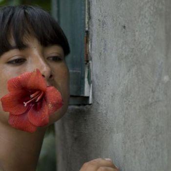 Film still from Milk of Sorrow (young woman with hibiscus in her mouth, standing by wall)