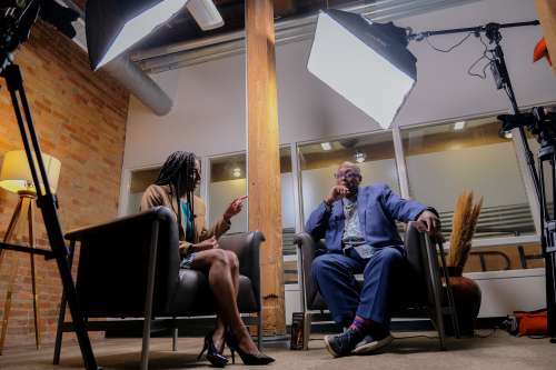 a Black man and woman in deep discussion with studio lights hanging overhead