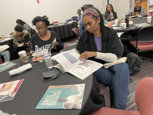 two women flip through SNCC toolkits while sitting at a table
